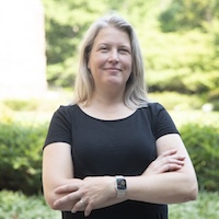 Emily Bernhardt standing in black short-sleeved shirt with her arms crossed. Bernhardt is the James B. Duke Distinguished Professor of Biology.