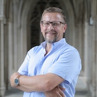 Norman Wirzba standing with arms folded and in a blue, short-sleeved shirt. Looking directly at the camera and smiling. Wirzba is the Gilbert T. Rowe Distinguished Professor of Christian Theology; a senior fellow at the Kenan Institute for Ethics; and the director of research for the Office of Climate and Sustainability.